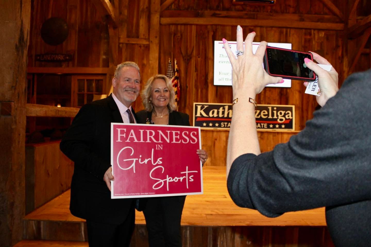 Kathy Szeliga and a supporter holding a Fairness in Girls Sports sign while a guest takes their photo.